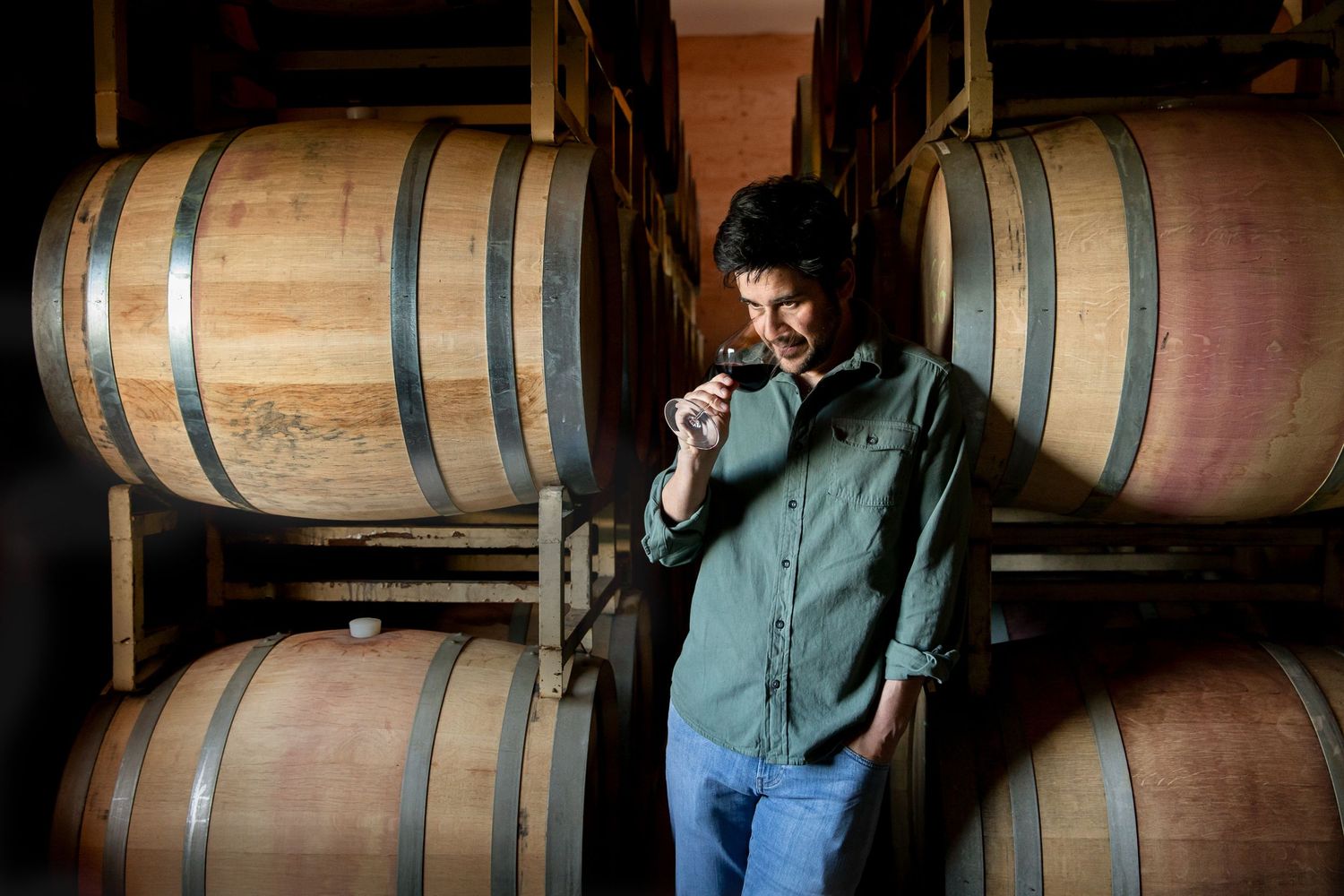 Wine barrels stacked in a rustic cellar with dramatic lighting and wooden details.