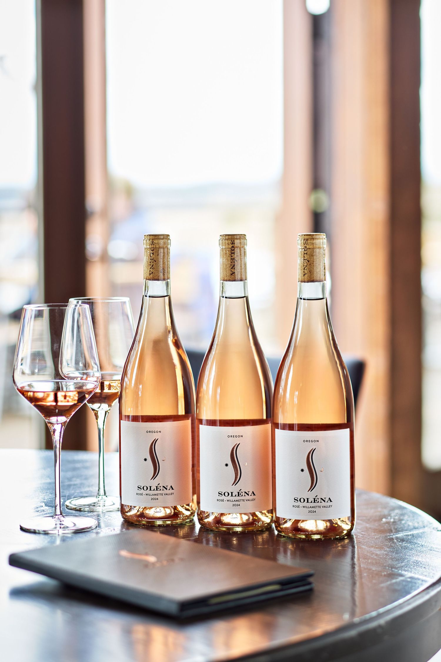 Three bottles of rose wine with matching wine glasses on table at tasting room.