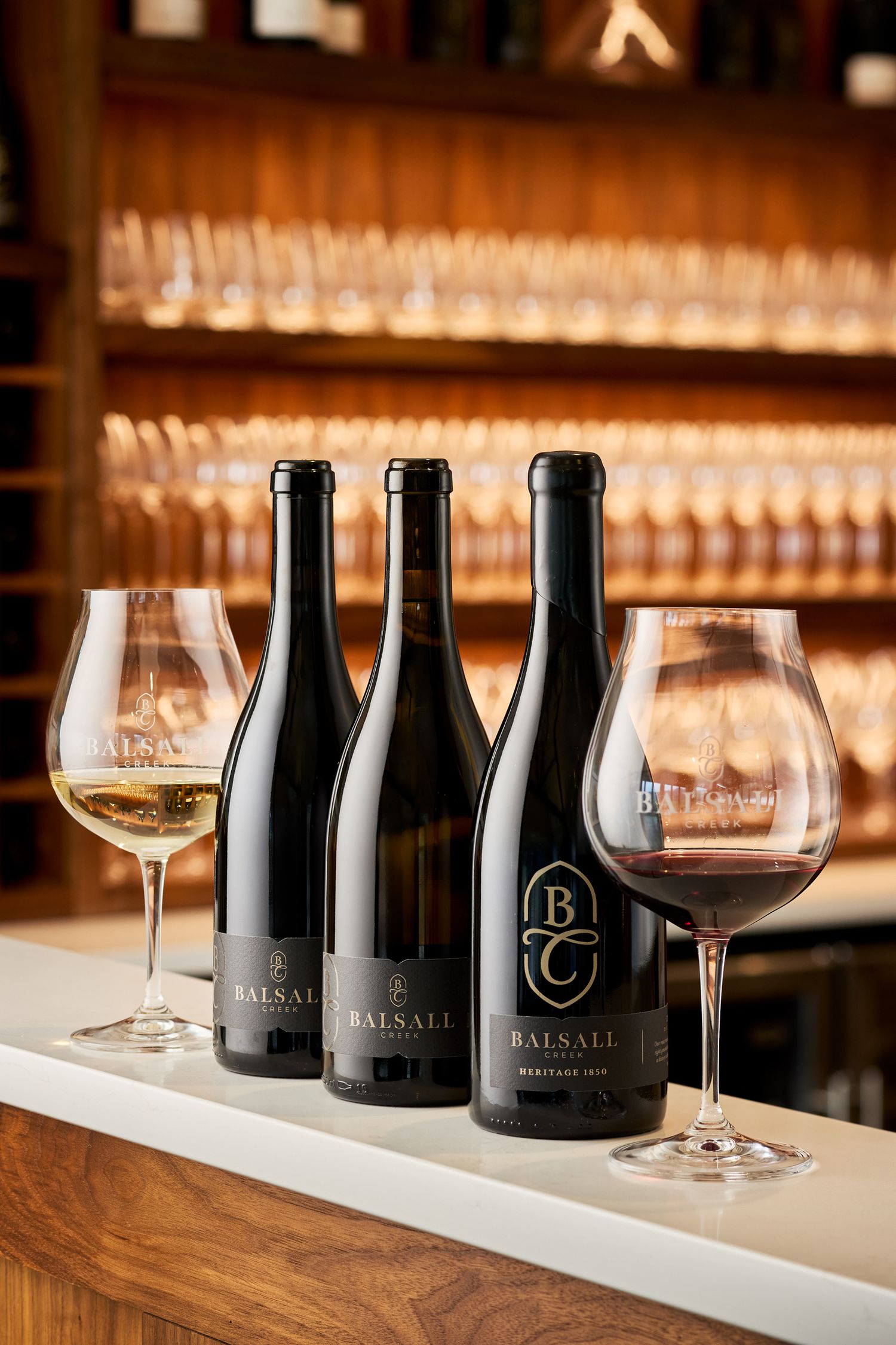 Dark wine bottles and glasses arranged for tasting on wooden bar counter.