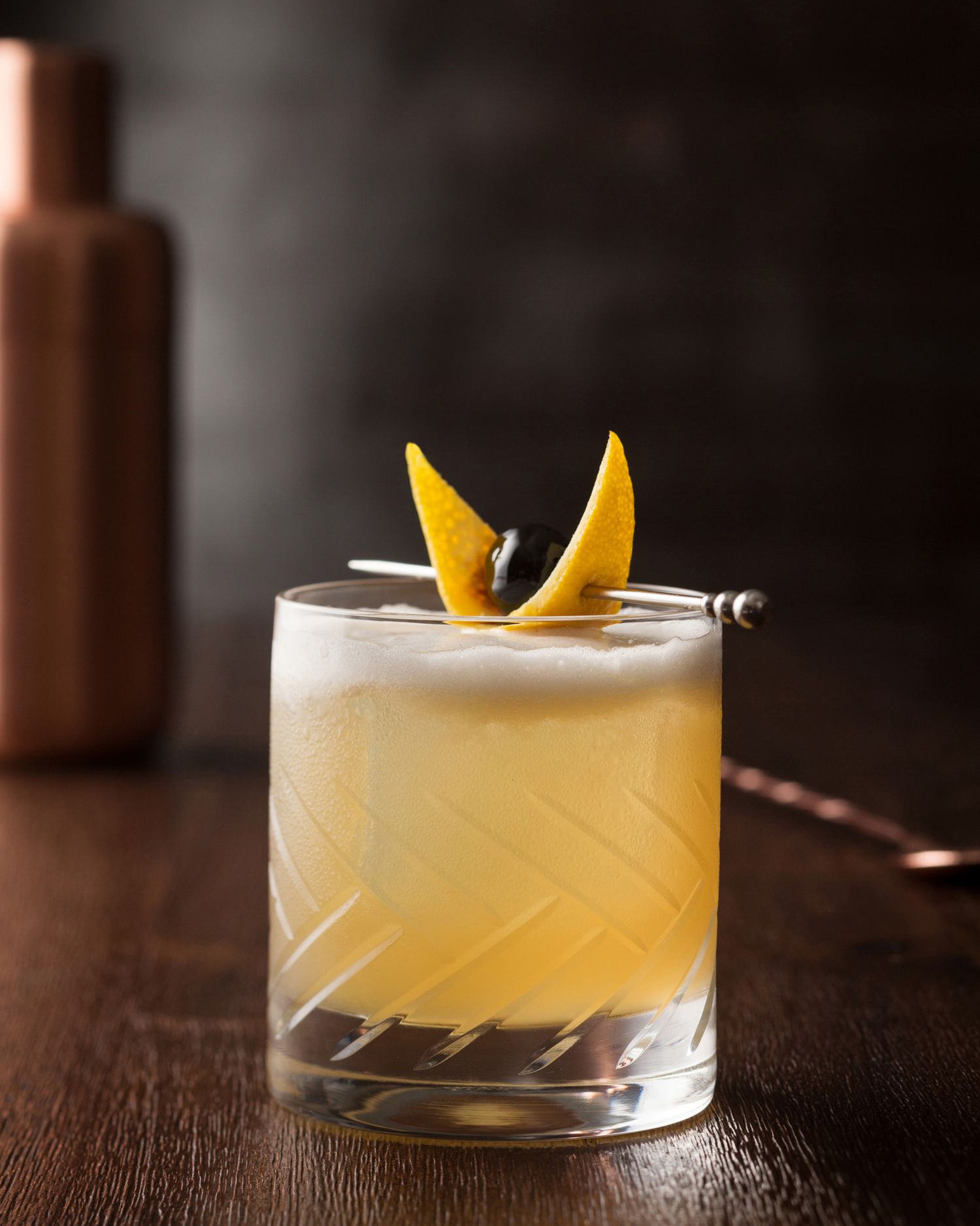Citrus-garnished cocktail with orange peel in crystal glass on dark wooden surface.