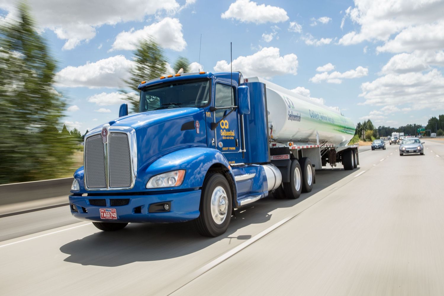 Blue semi trucks driving on highway under cloudy summer sky.