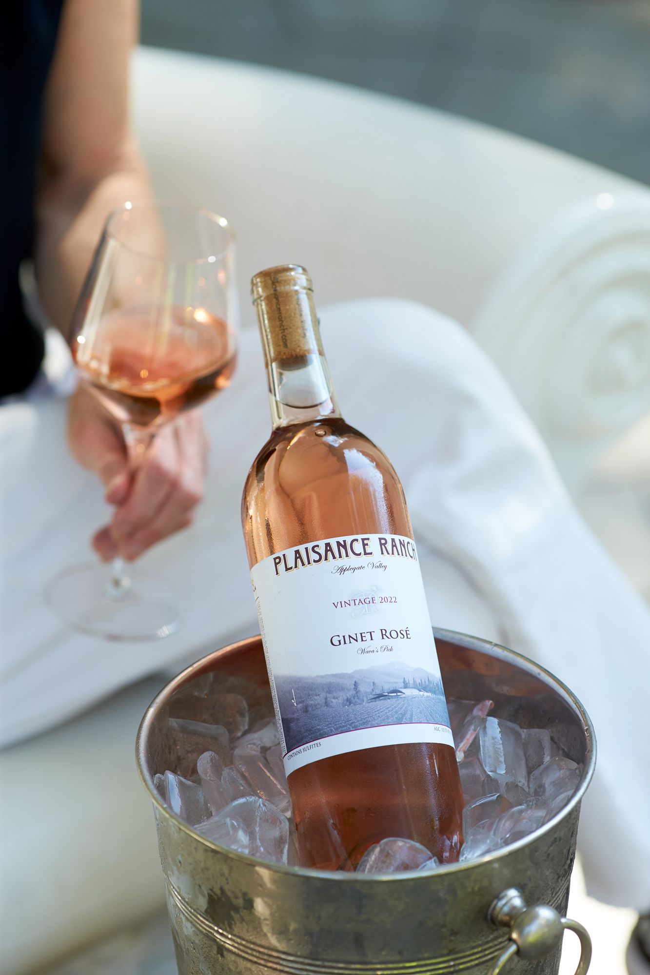 Plaisance Ranch Ginet Rosé wine bottle chilling in ice bucket with a glass of rosé wine held nearby.
