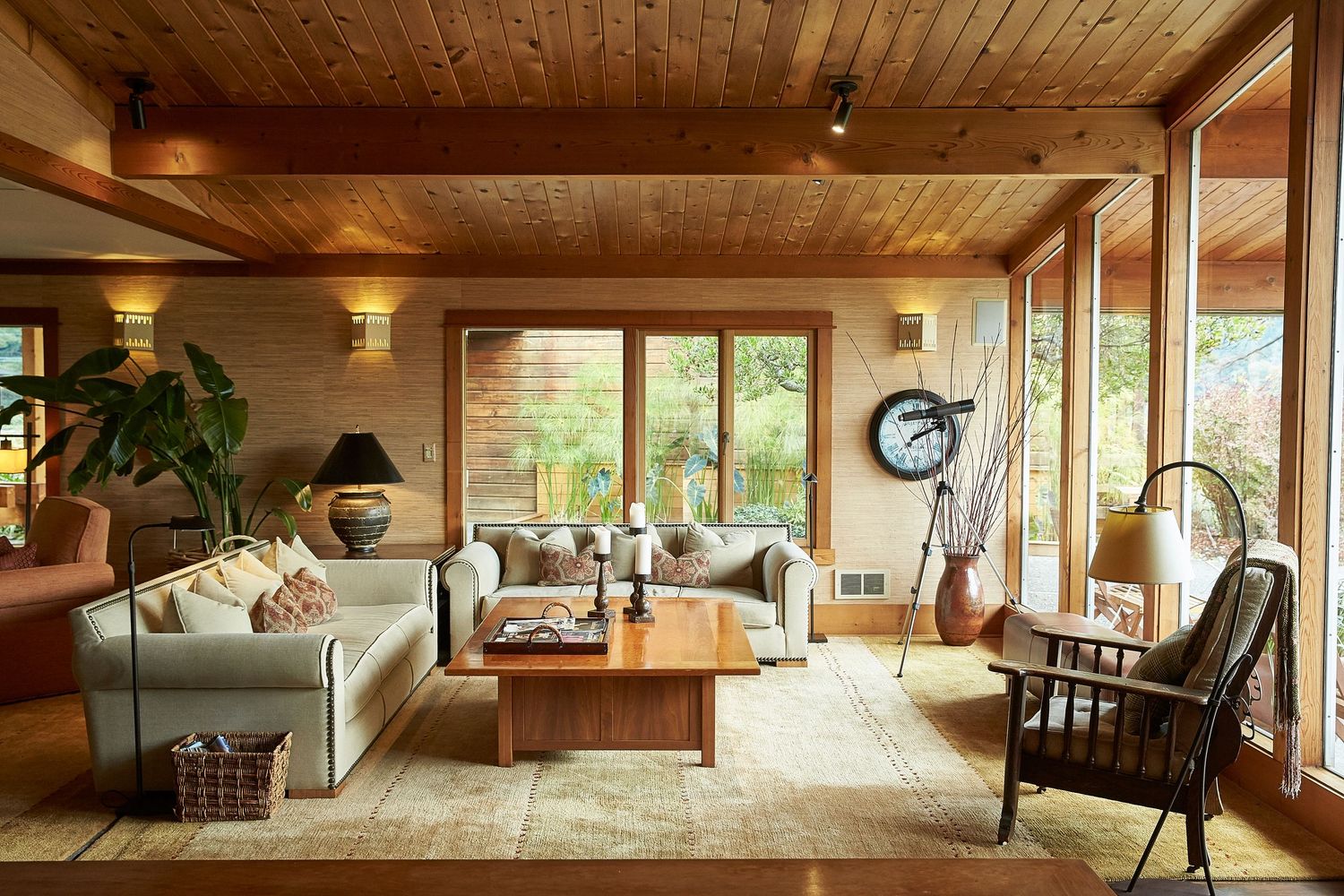 Cozy living room with wood-paneled ceiling, large windows, and comfortable seating arrangements.