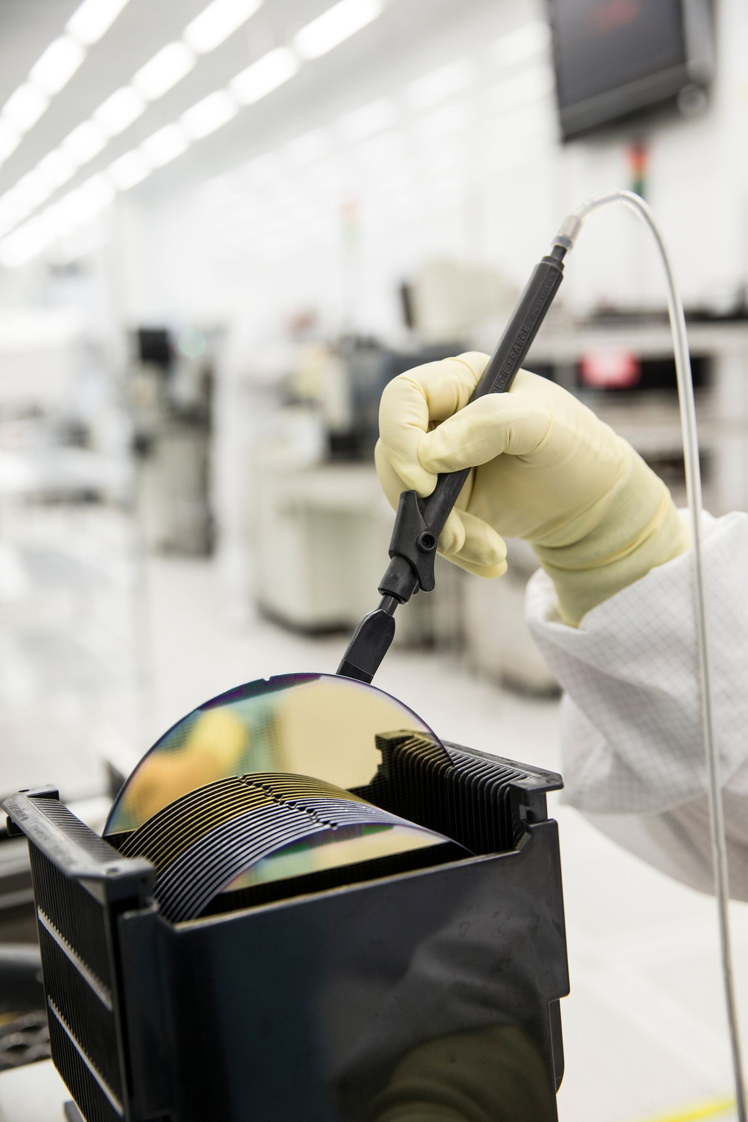 Gloved hand uses precision tool on semiconductor wafer in clean room environment.
