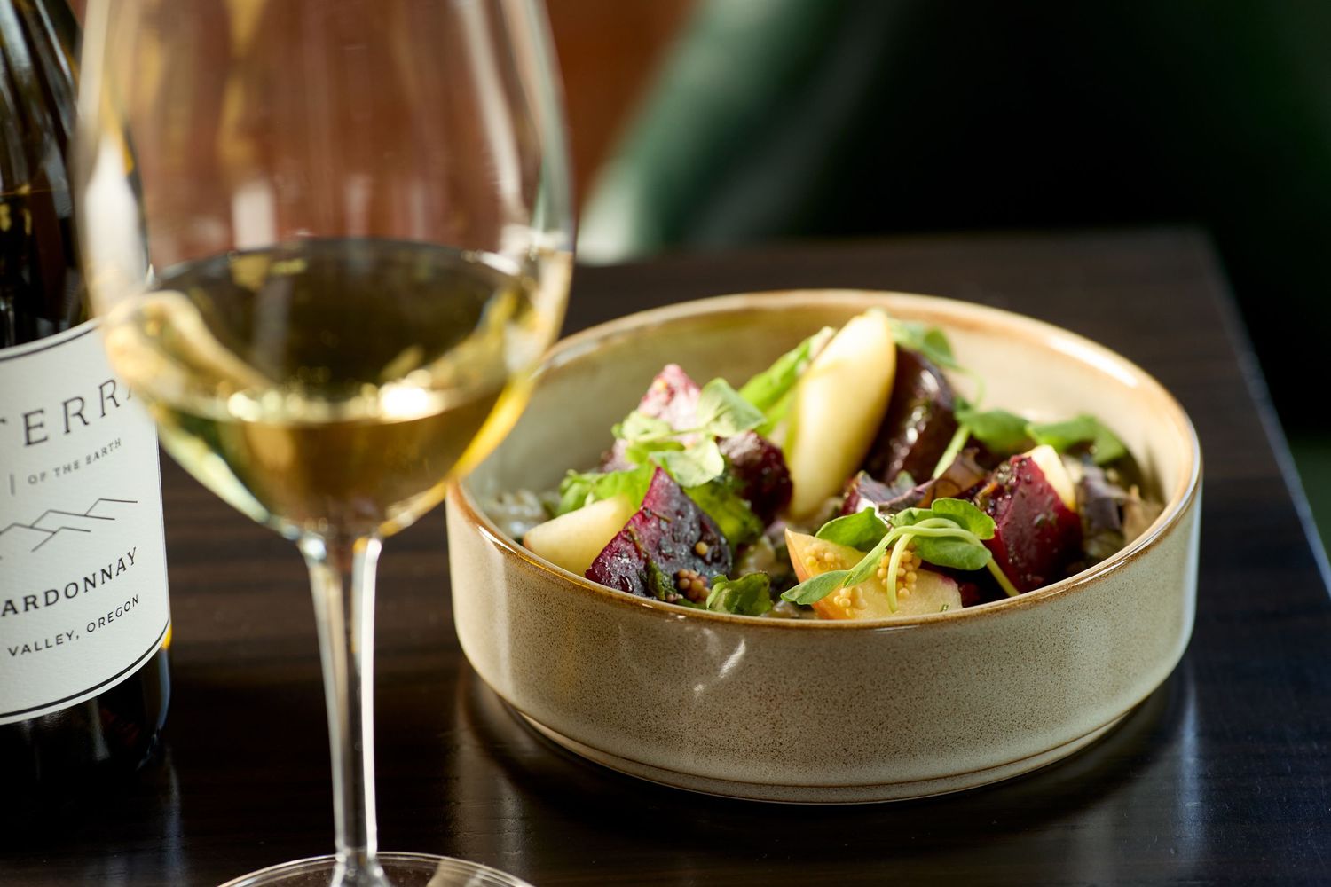 Fine dining plates with colorful salads and wine glasses arranged on a dark table.