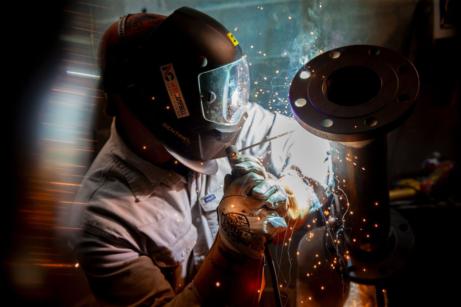 Welder working with sparks flying in a dark workshop environment.