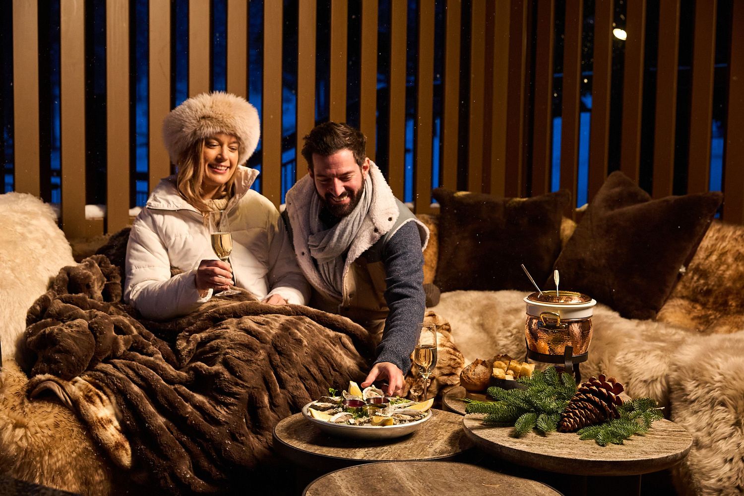 People gather around a rustic wooden table for a cozy dinner party in a warmly lit cabin setting.