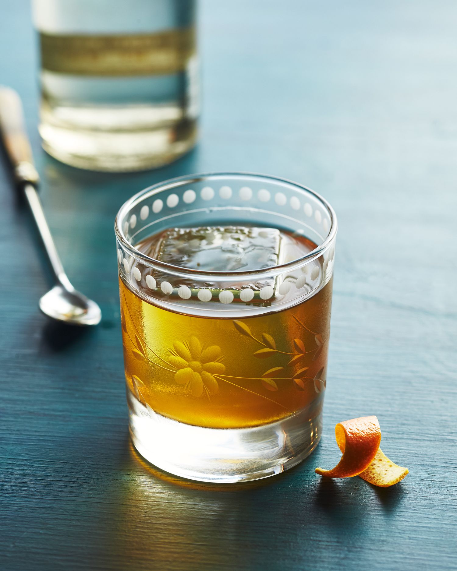 Crystal cocktail glasses filled with amber-colored drinks garnished with orange peel on a blue surface.