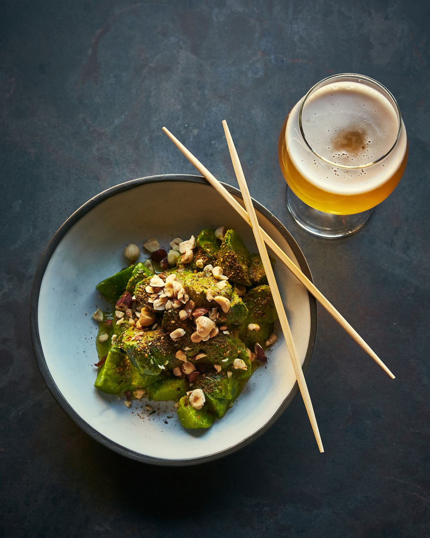 Asian-inspired salad with chopsticks and beer served in a blue ceramic bowl on dark background.