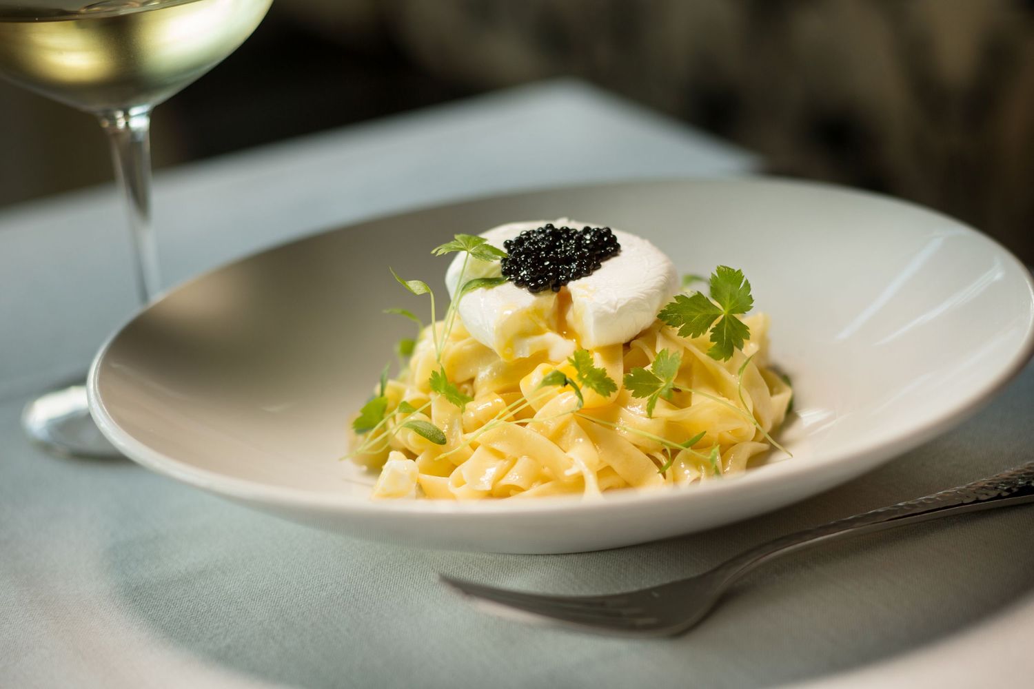 Elegant pasta dish topped with caviar and microgreens in a white bowl.