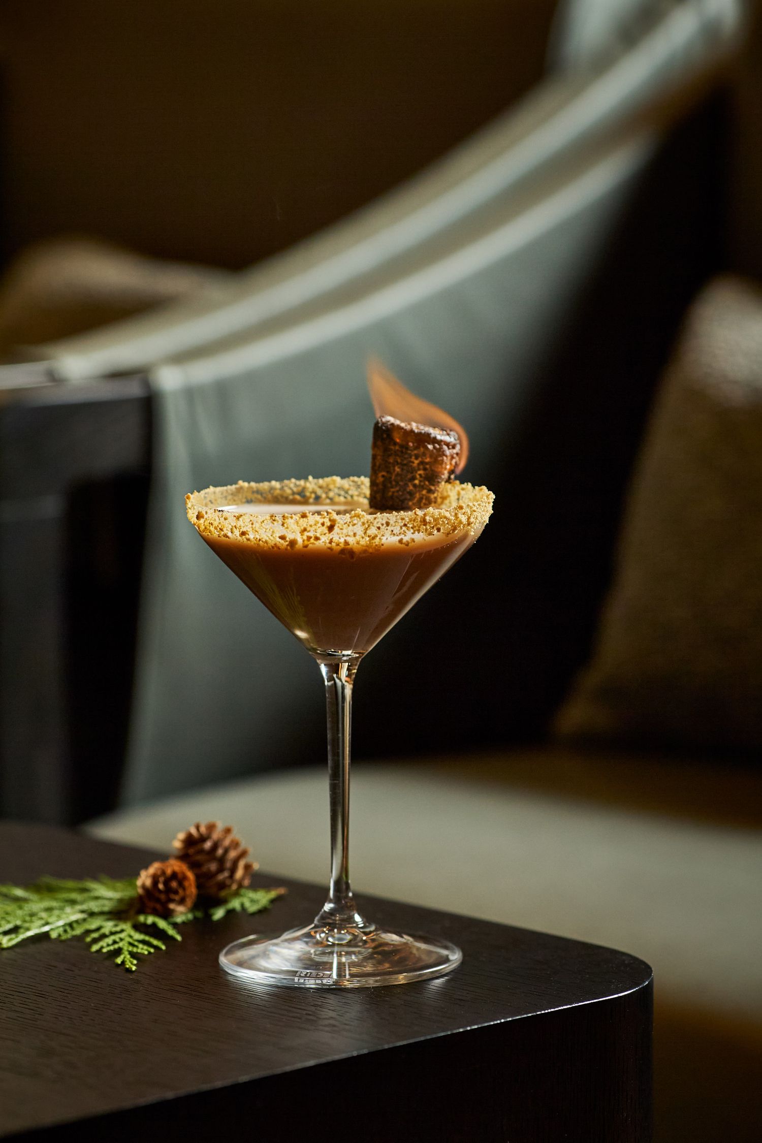 A chocolate espresso martini cocktail garnished with a biscotti cookie in a coupe glass against a dark background.