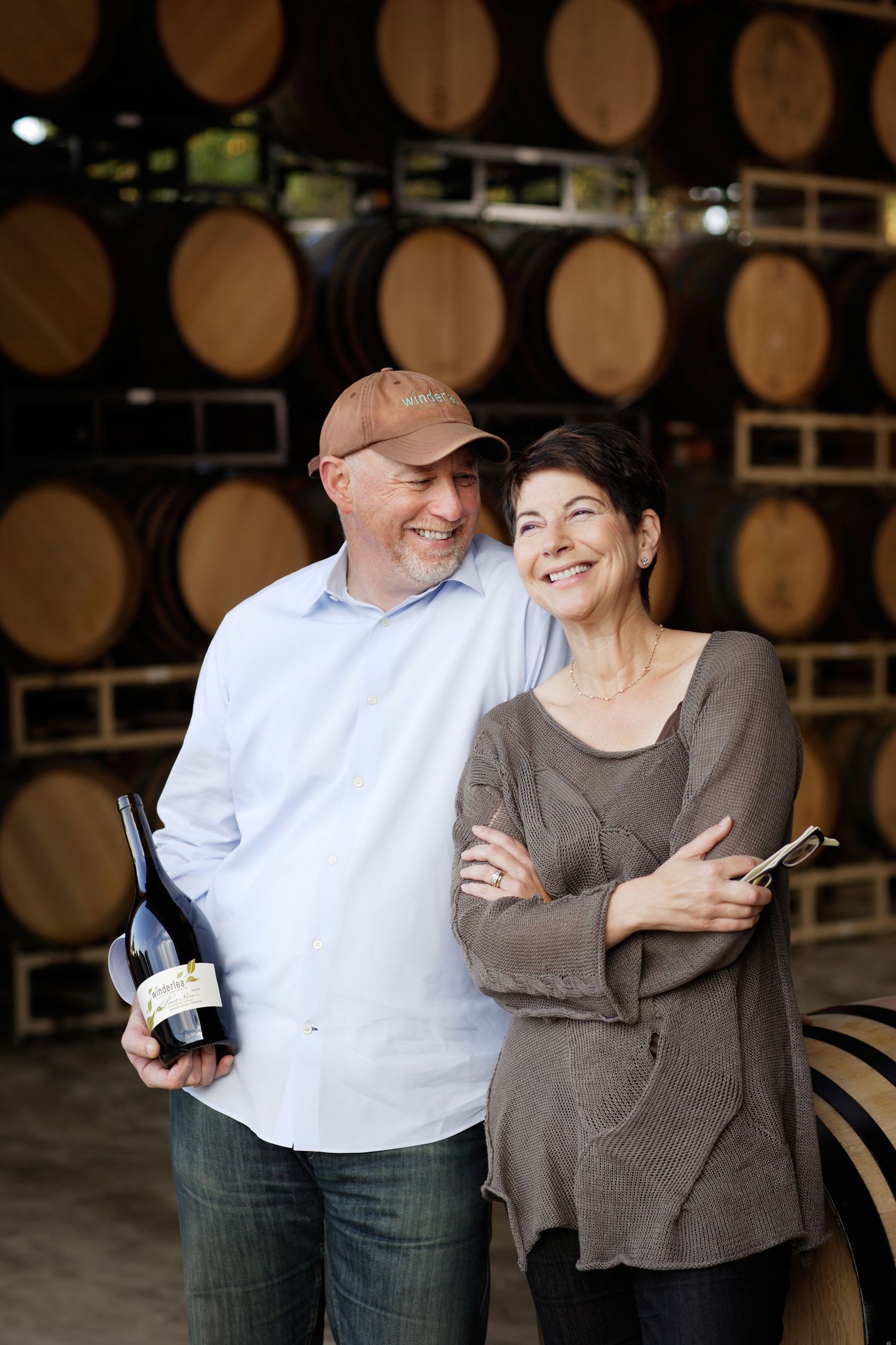 Couple sharing a moment in a wine cellar with wooden barrels in the background.