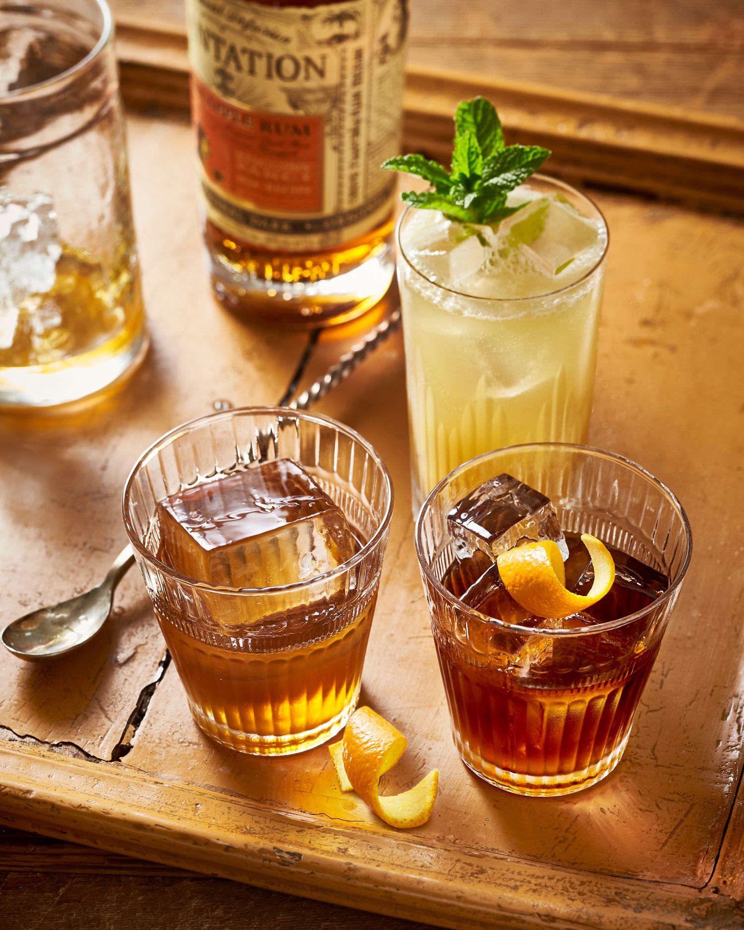 Elegant craft cocktails with citrus garnishes served in vintage glassware on a wooden bar surface.