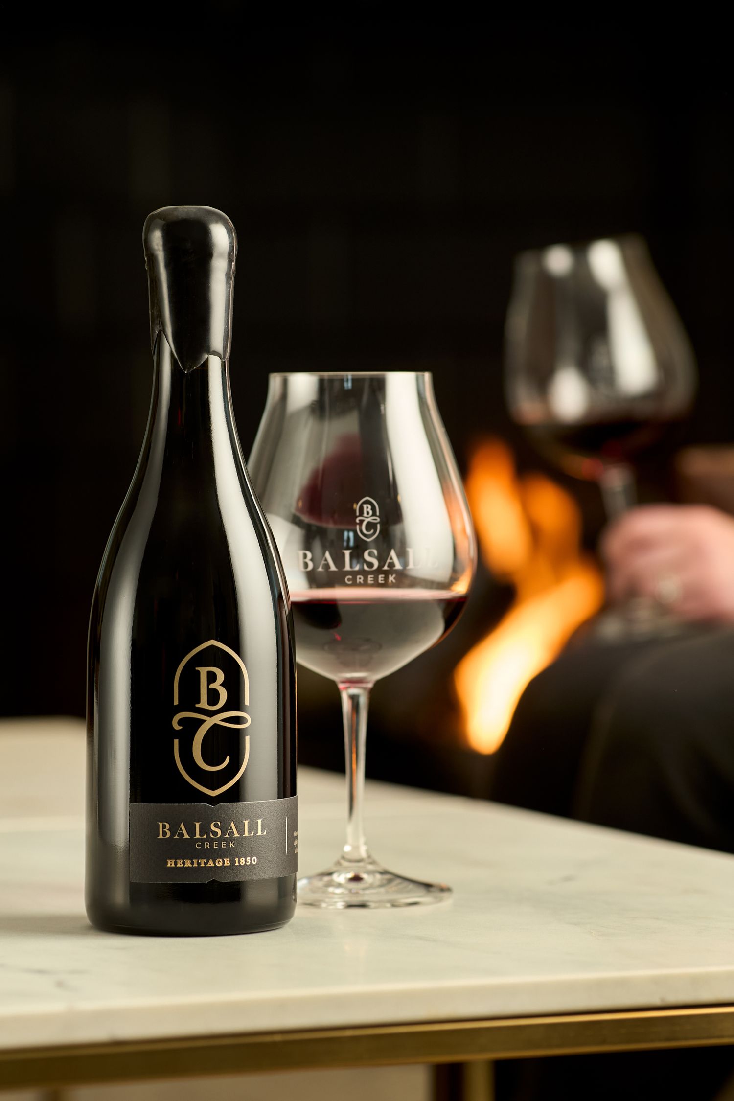 Elegant black wine bottles and branded glasses arranged on white surface with warm lighting.
