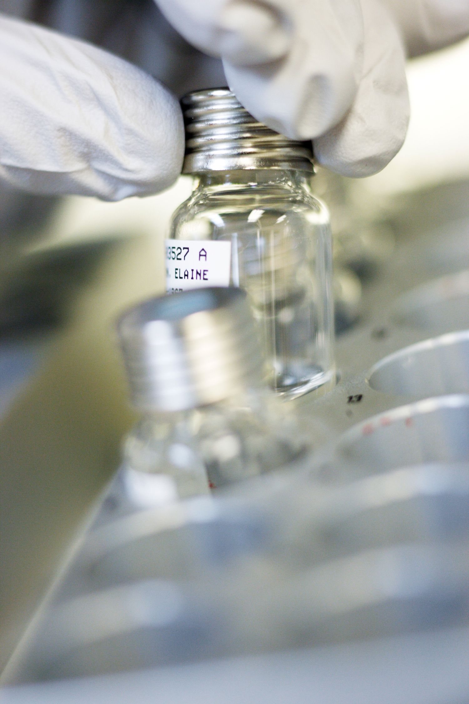 Close-up of gloved hands handling medical vials in laboratory setting.