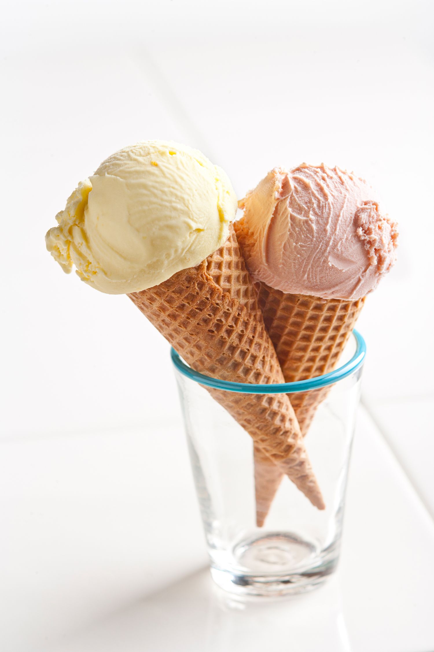 Ice cream cones with vanilla and strawberry scoops arranged in clear glass holders against white background.