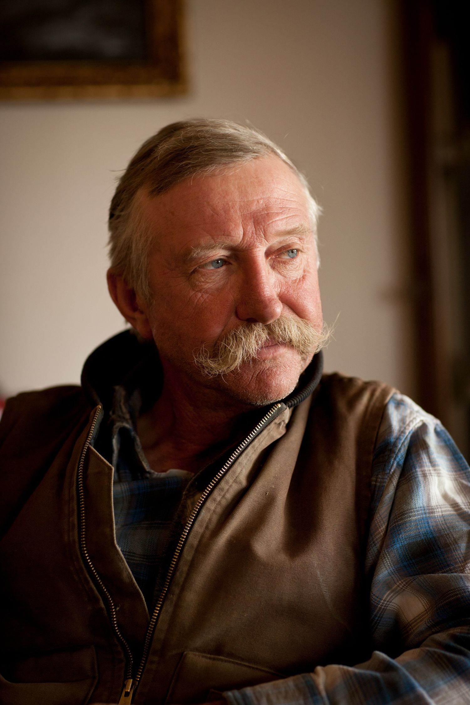 A close-up portrait showing a weathered face with a distinctive mustache.