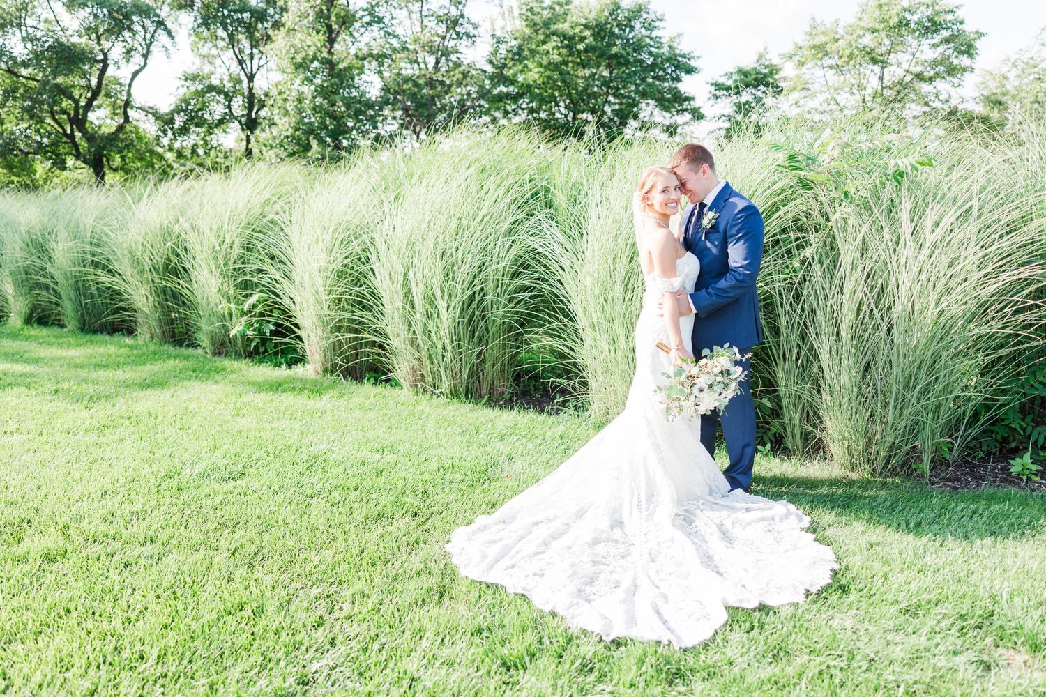 Newlyweds sharing intimate moment by ornamental grasses in garden setting.