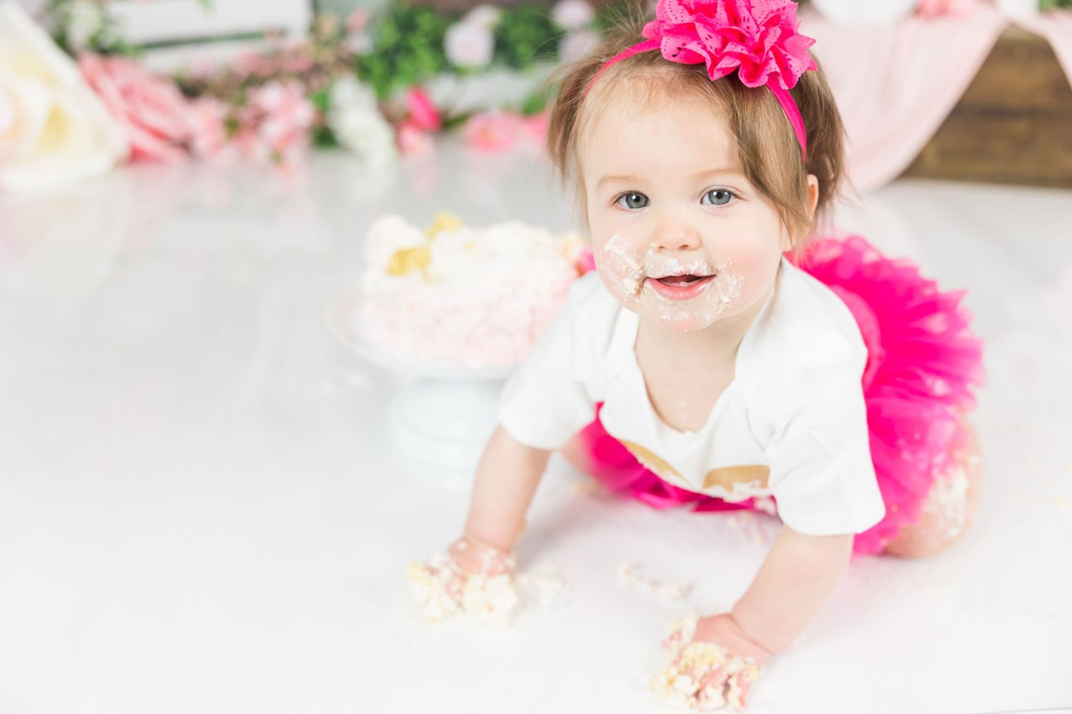 Baby portrait with pink tutu and floral decorations against white backdrop.