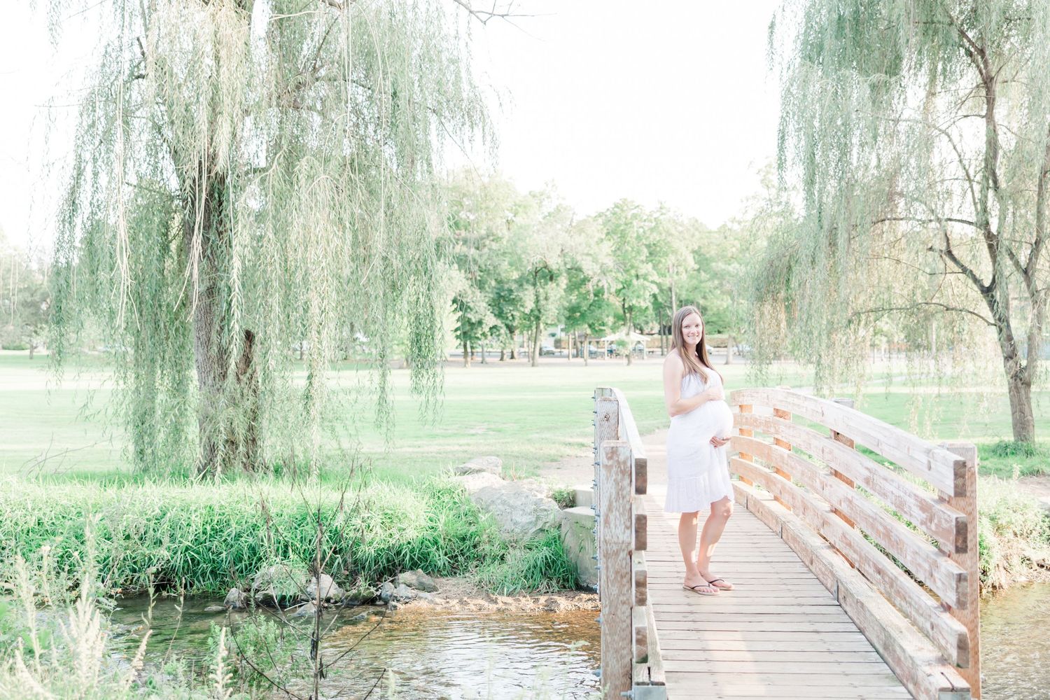 Romantic bridge scene with willow trees and water in soft pastel tones.