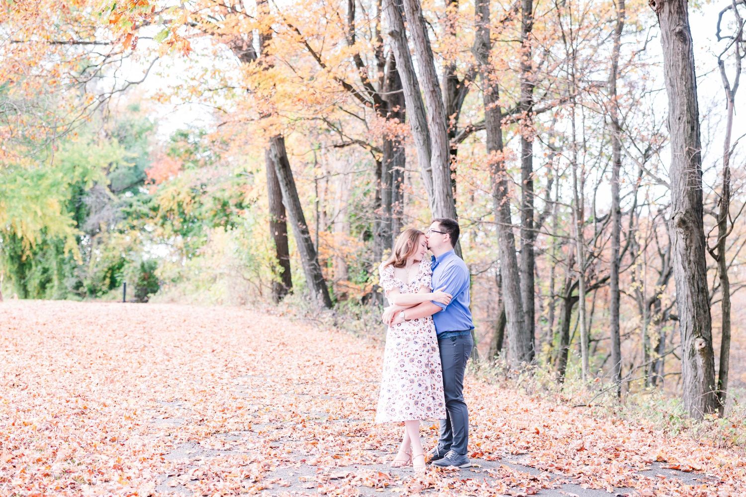 A romantic autumn engagement photo showing a couple embracing on a path covered with fallen leaves.
