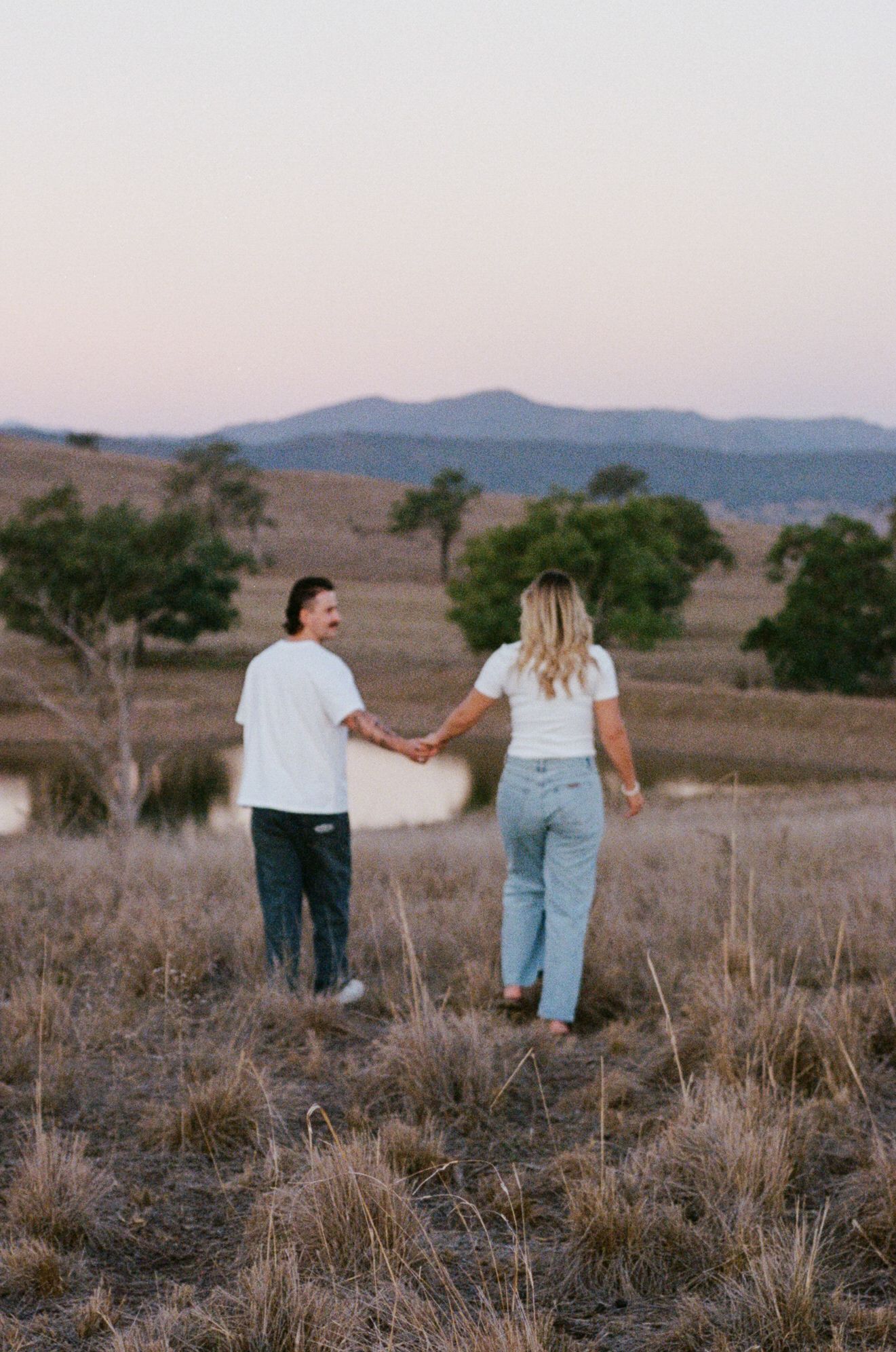 couple walking through paddock holding hands during Scone engagement photoshoot