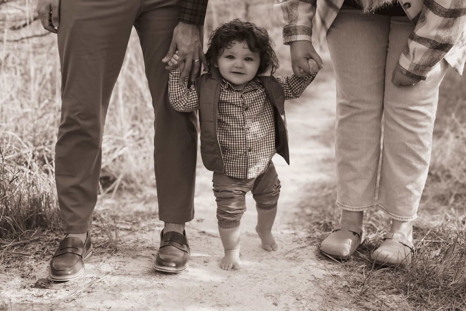 Toddler standing between his parents legs, smiling during a family session at Oakes Quarry in Fairborn, OH. Photographed by Vicci Photo
