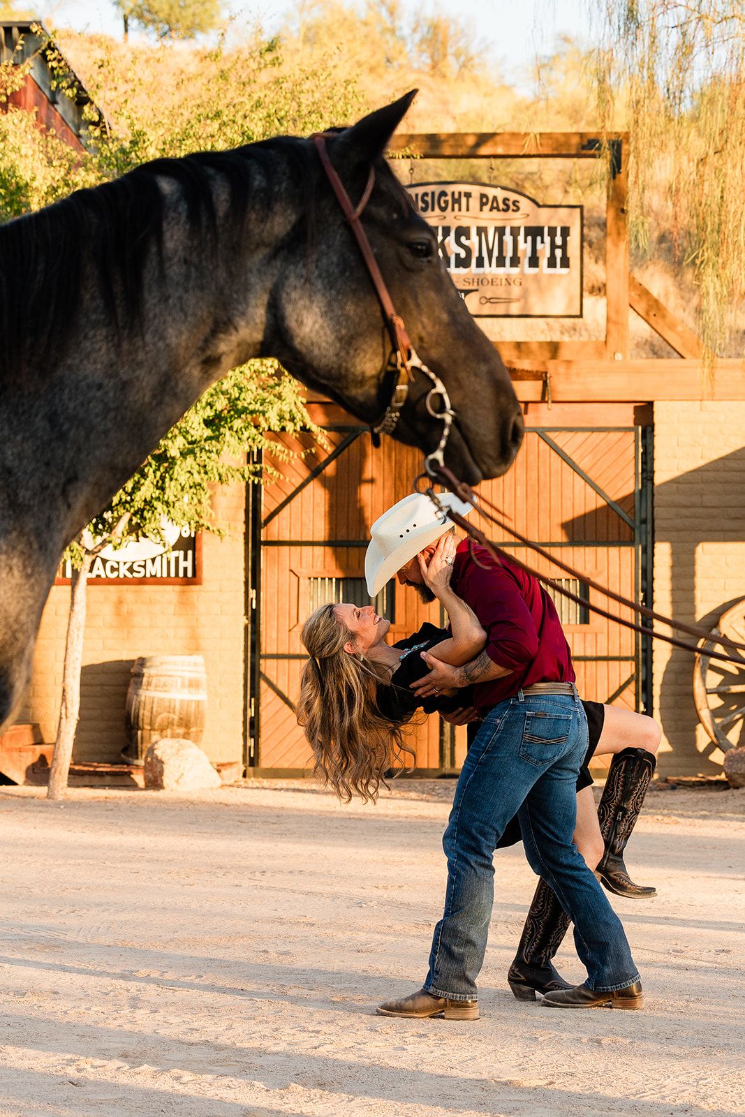 A black horse and an embrace in front of a rustic blacksmith shop during golden hour.