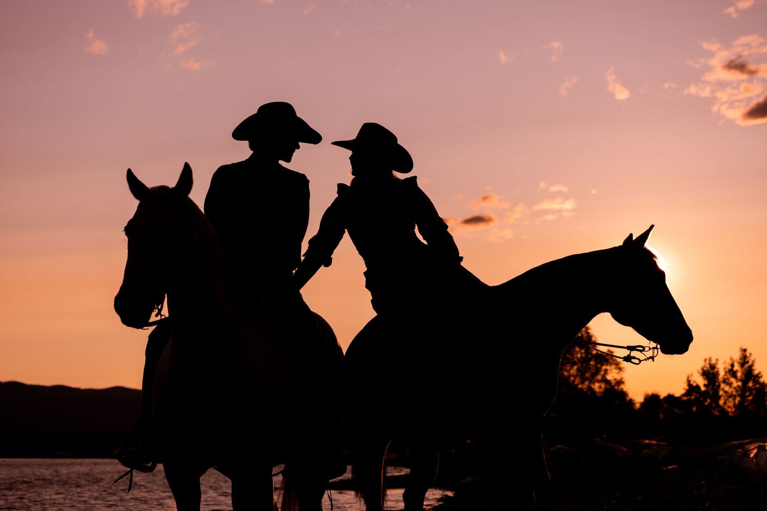 Silhouette of two riders on horseback against a dramatic sunset sky with orange clouds.