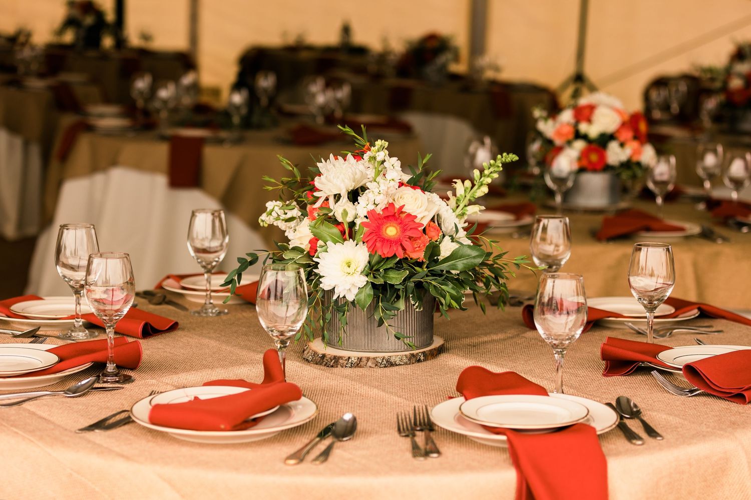 Elegant wedding reception table setting with red napkins and a centerpiece of coral and white flowers in a silver vase.