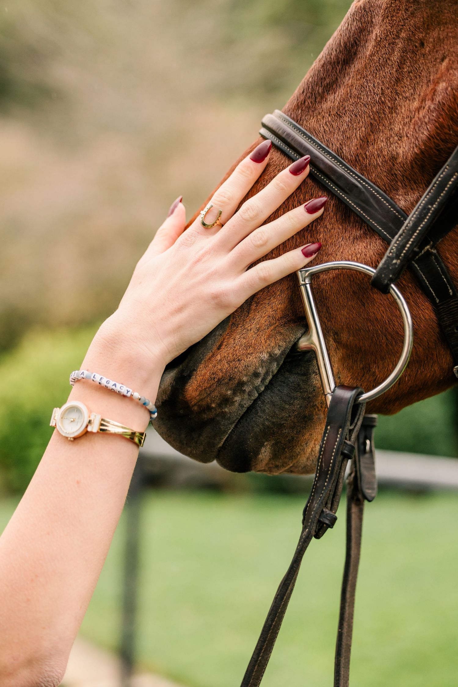 A hand wearing bracelets gently touches a brown horse's face near the bridle and bit.