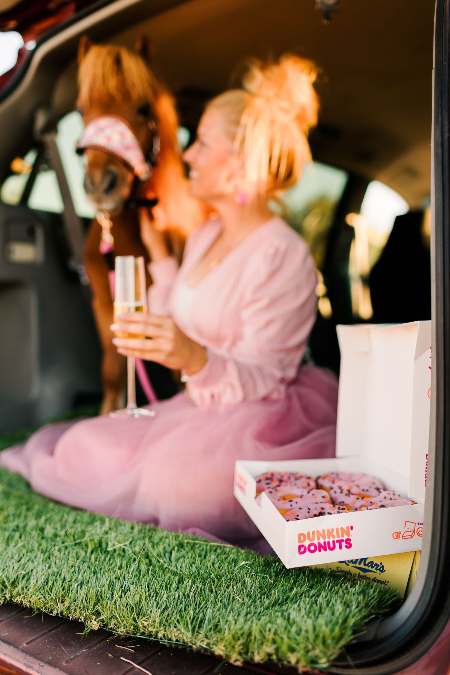 Pink-themed picnic setup in car trunk with donuts and artificial grass.