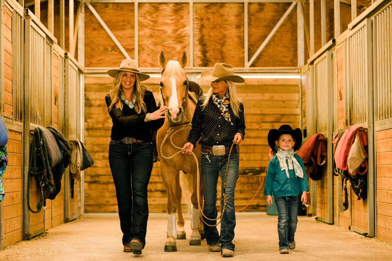 A group walks with a cream-colored horse down a wooden stable hallway.
