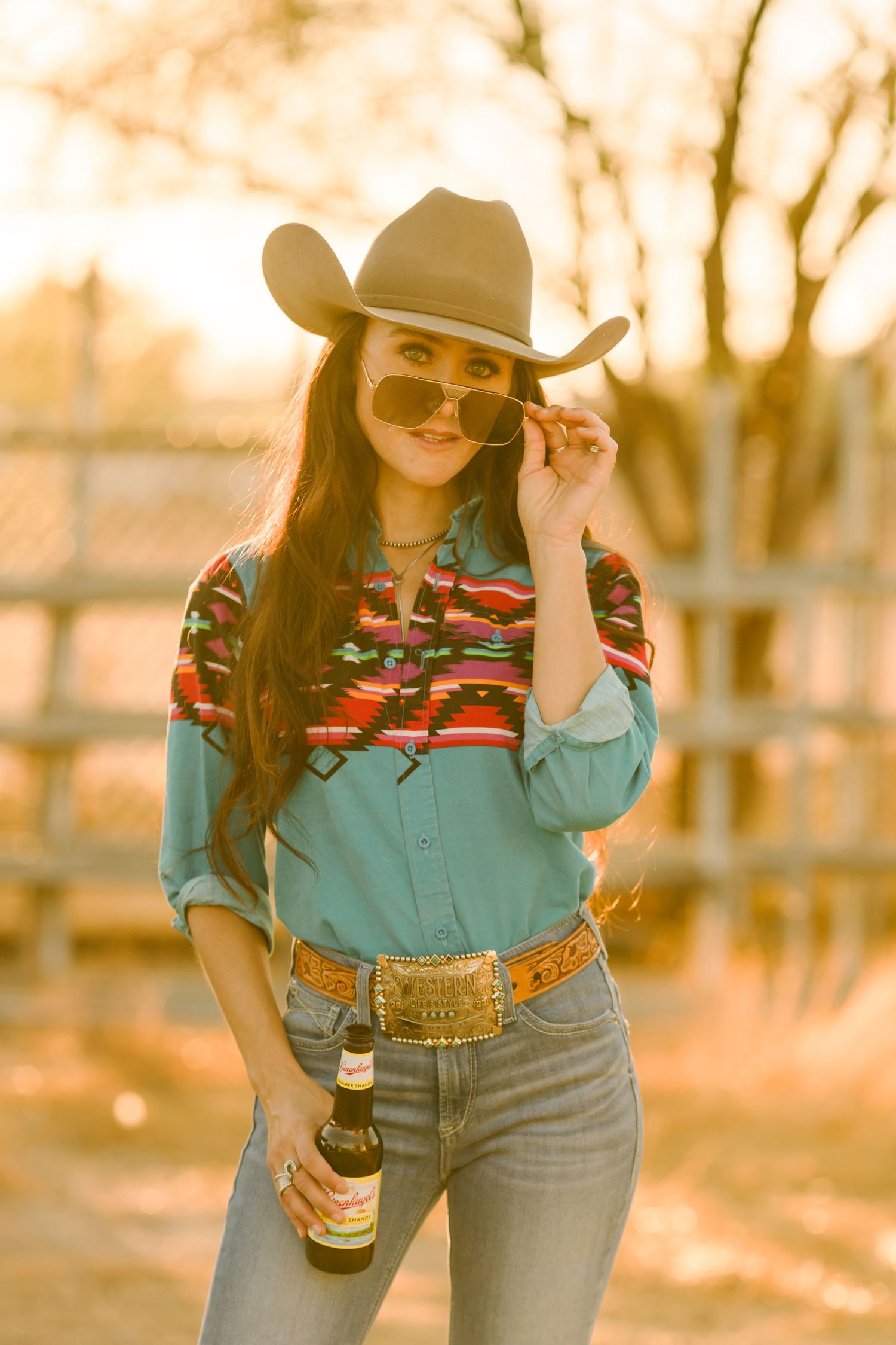 Western style outfit with cowboy hat, denim and colorful retro shirt in warm sunset lighting.