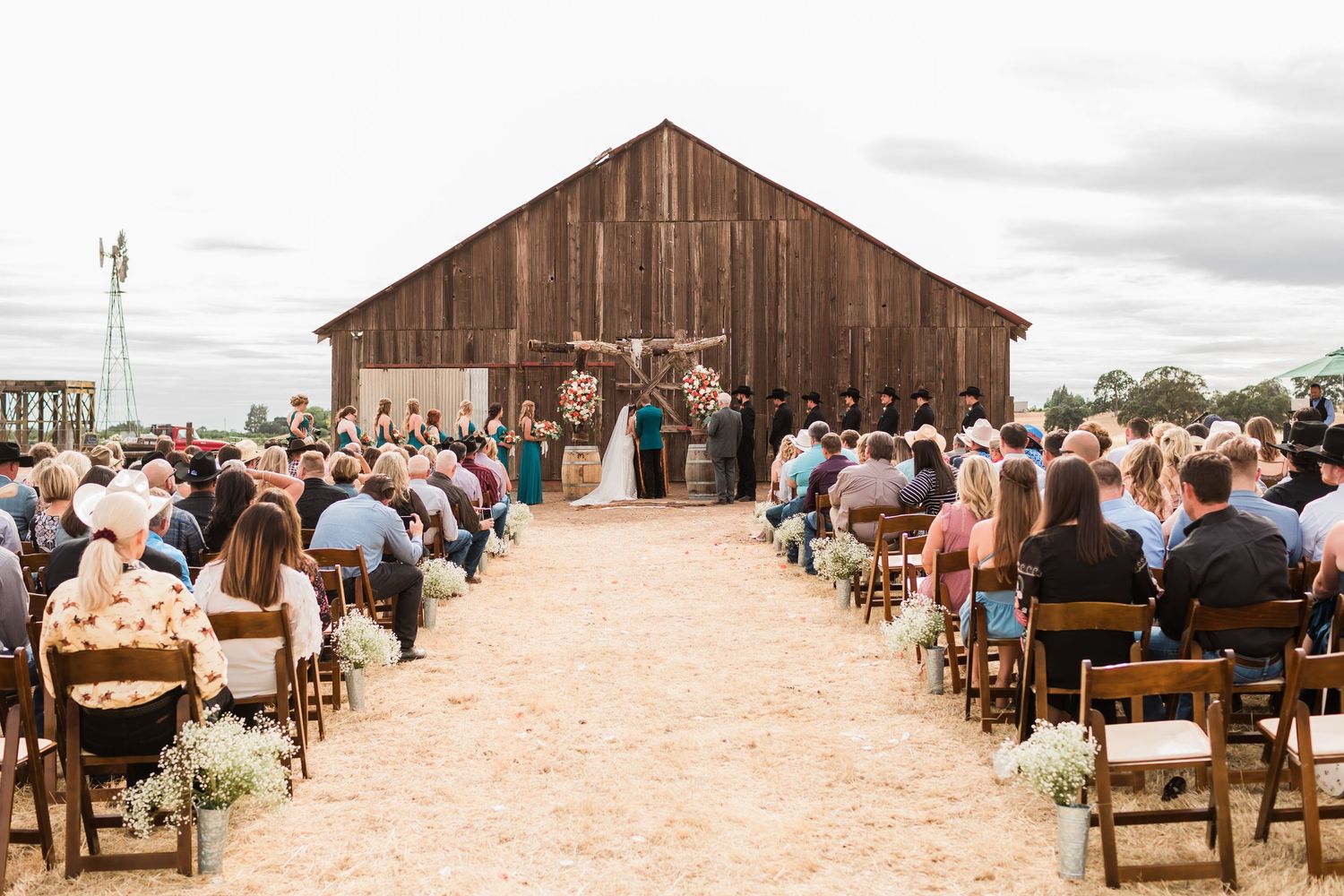 A rustic outdoor wedding ceremony in progress with wooden chairs and guests seated on a ranch.