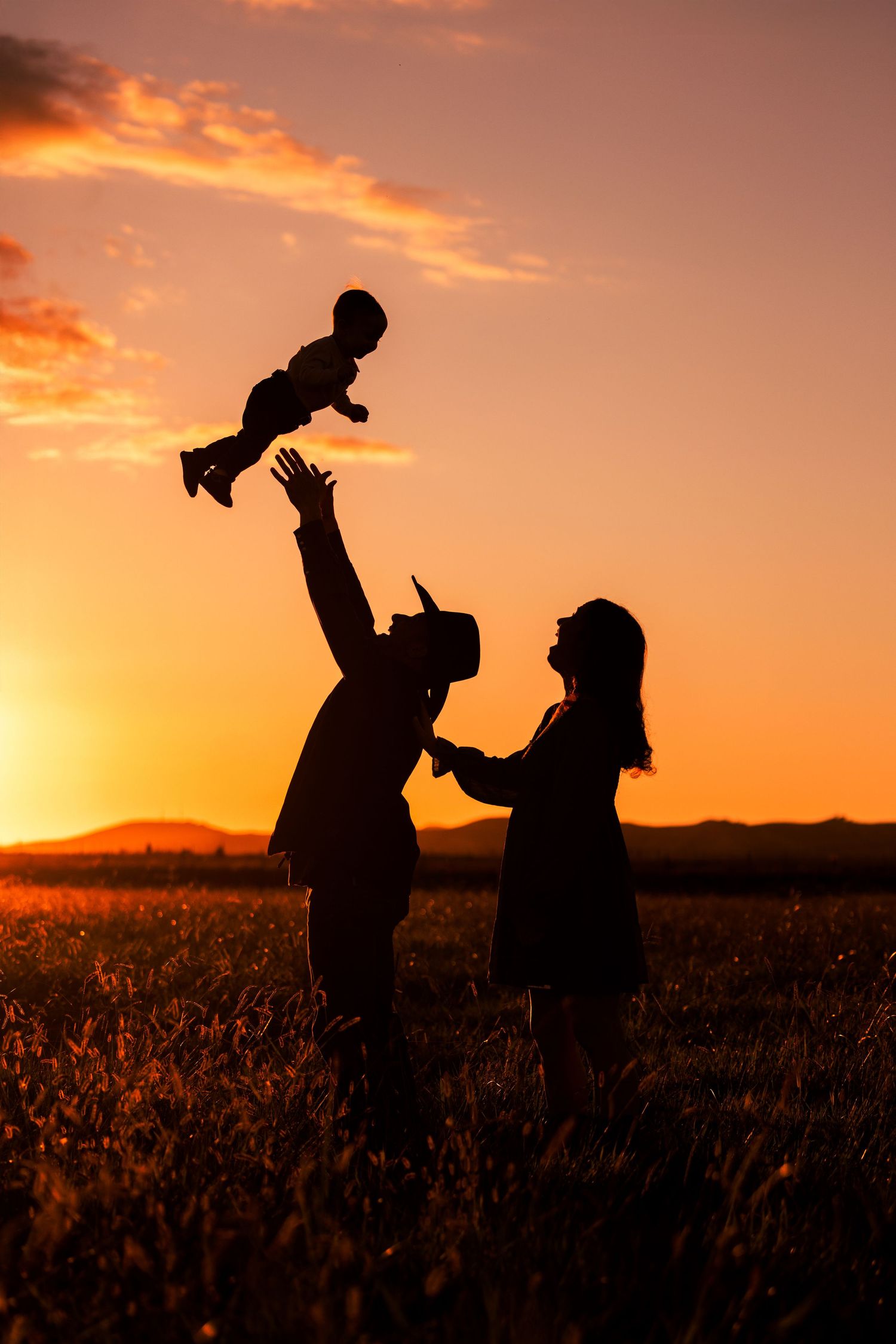 Silhouettes of two people playing and dancing together in a field during a vibrant orange sunset.
