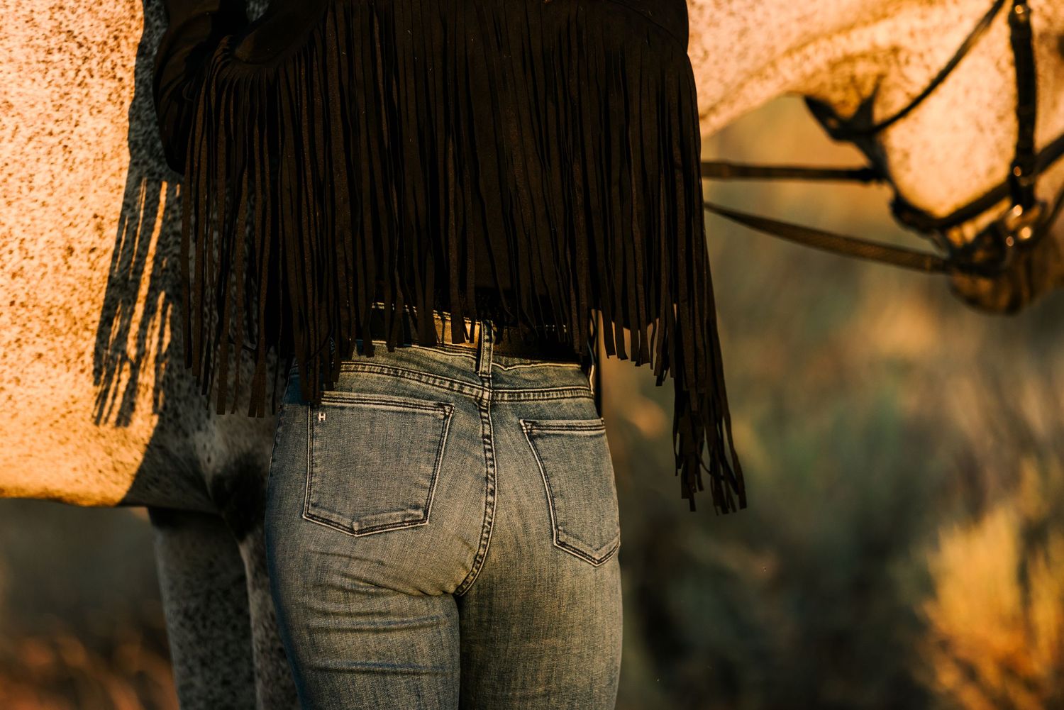 Close-up of fringe leather chaps and denim jeans in warm sunset lighting.