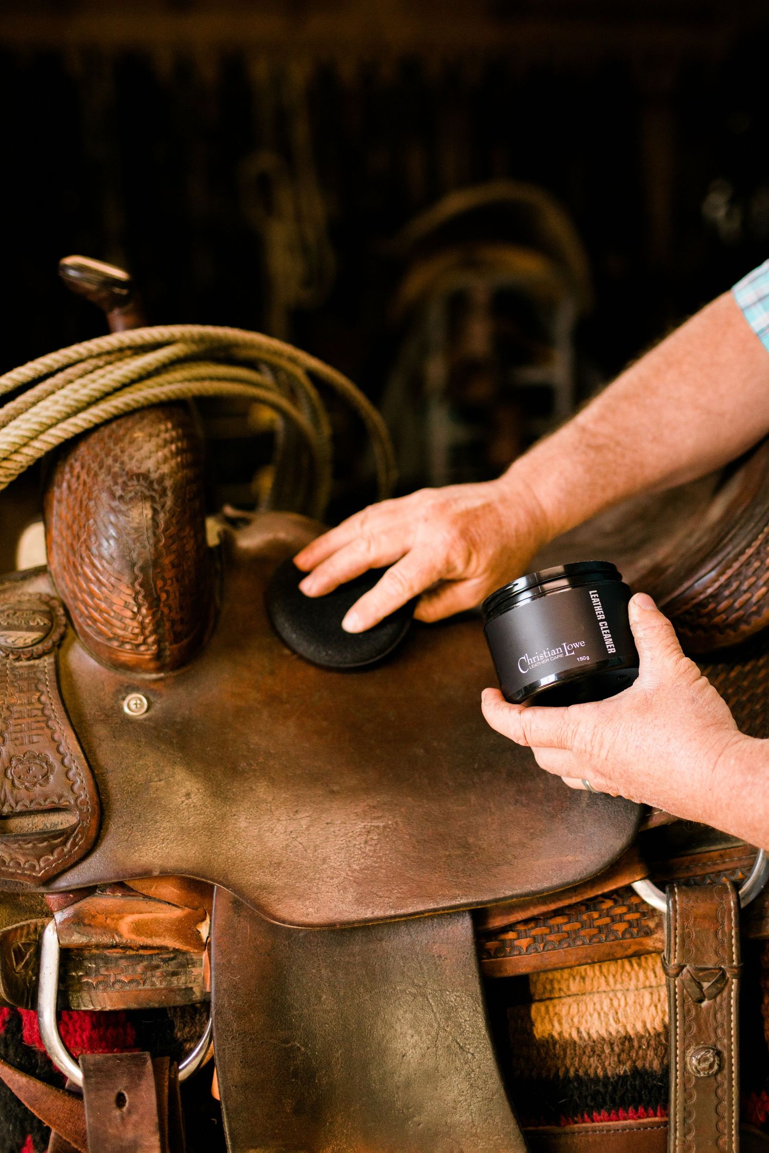 Close-up of hands applying leather conditioner to a western saddle.
