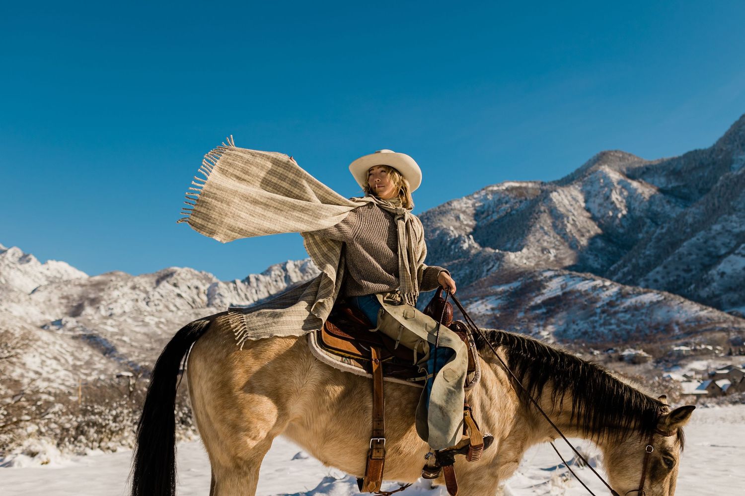 Cowboy riding horseback through snowy mountains carrying a newspaper.