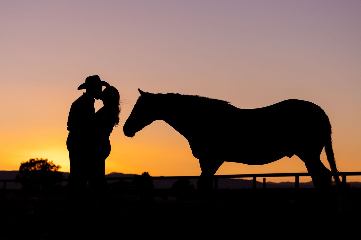 Silhouettes of a couple and horse stand against vibrant orange sunset sky in romantic western scene.