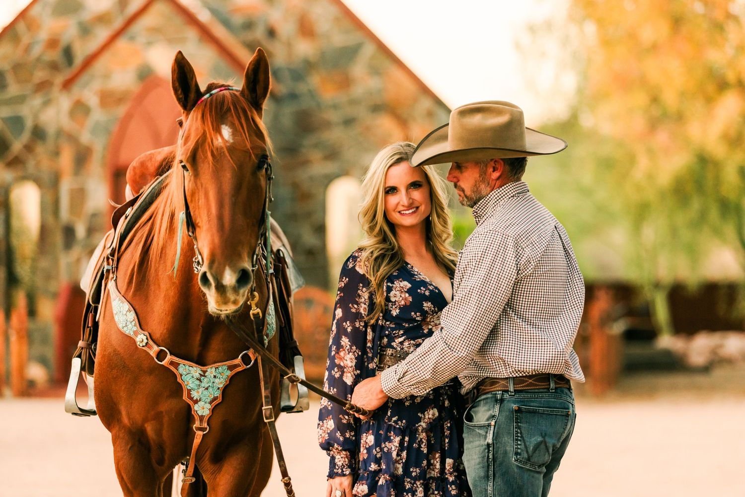 A romantic couple poses with their chestnut horse during a golden hour engagement photo session in autumn.