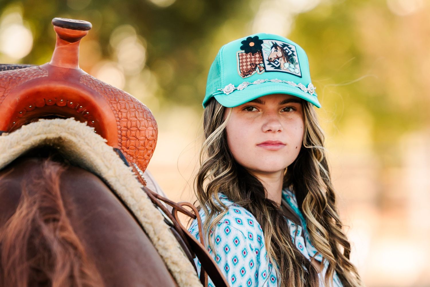 Young equestrian in a turquoise cap sitting beside a western saddle.