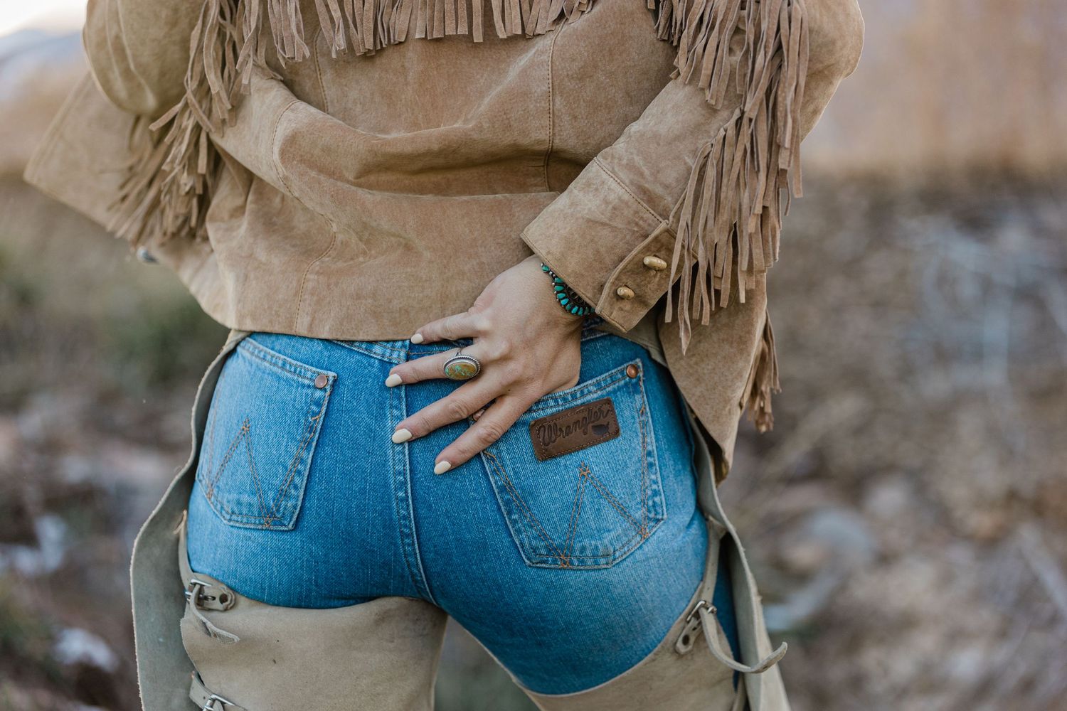 Close up of denim jeans with fringe leather chaps in rustic western style.
