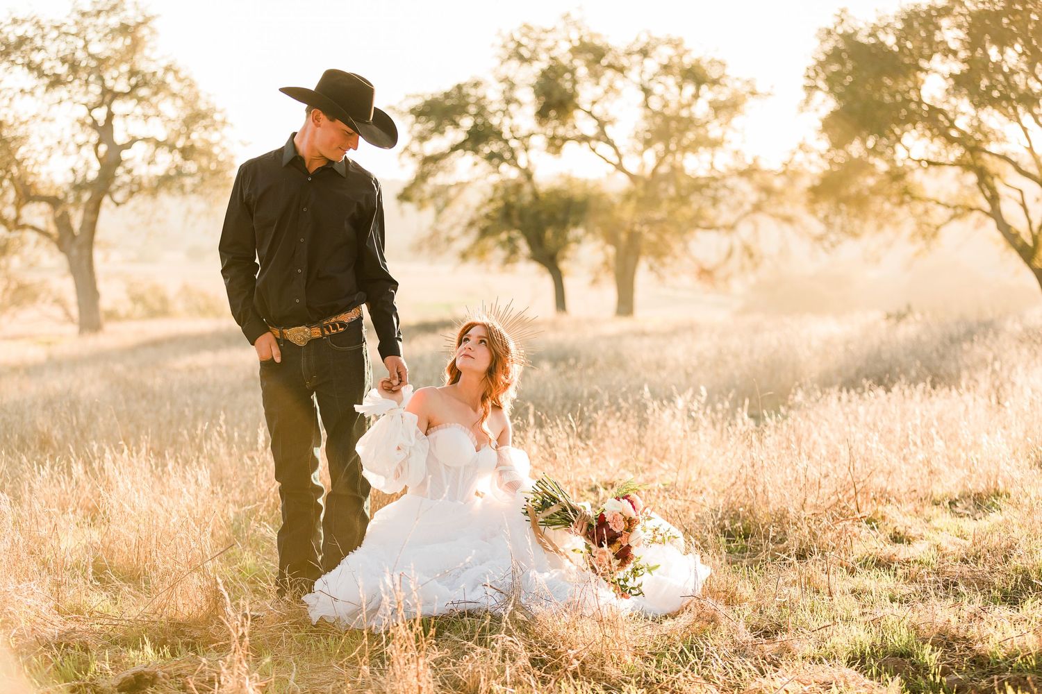 Romantic country wedding photoshoot in a golden field at sunset with flowing white dress and cowboy hat.
