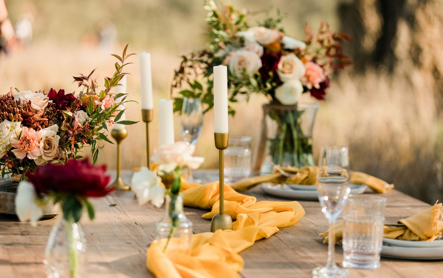 Romantic wedding table settings with golden table runners, floral centerpieces and elegant glassware in warm light.