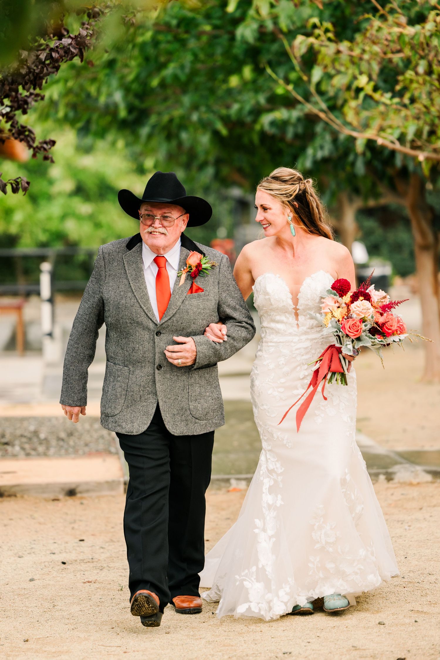 A couple shares a joyful moment walking together on a dirt path with trees in the background.