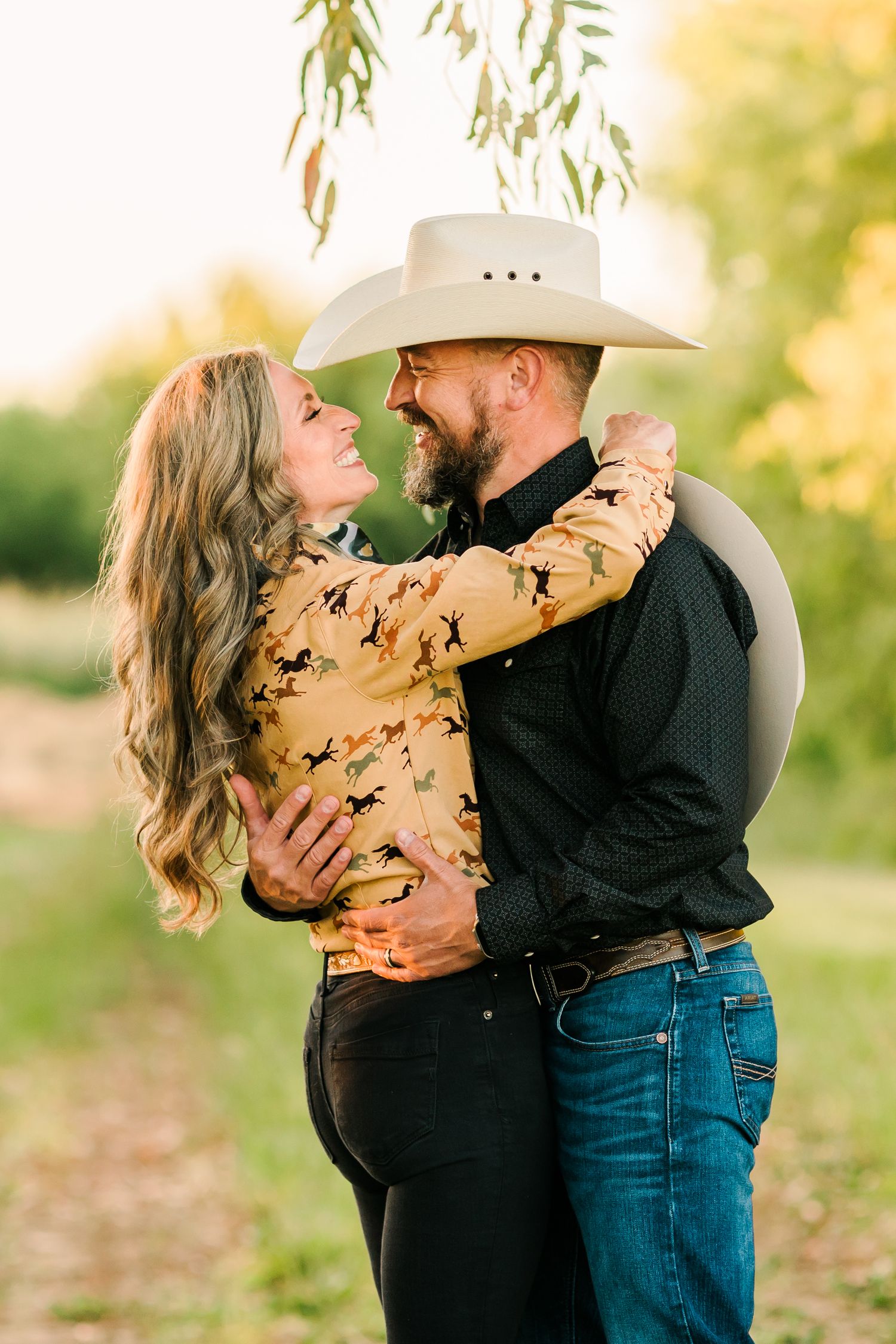 A couple embracing affectionately in a rural setting with a man wearing a cowboy hat.