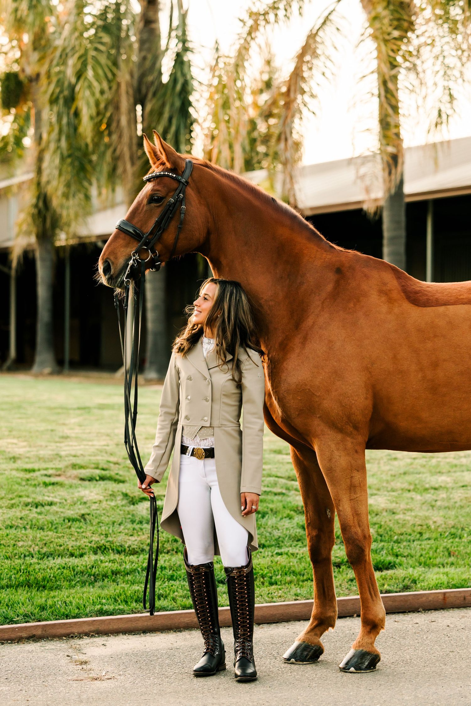 A chestnut brown horse stands with its handler on a gravel path beside a grassy area with trees in the background.