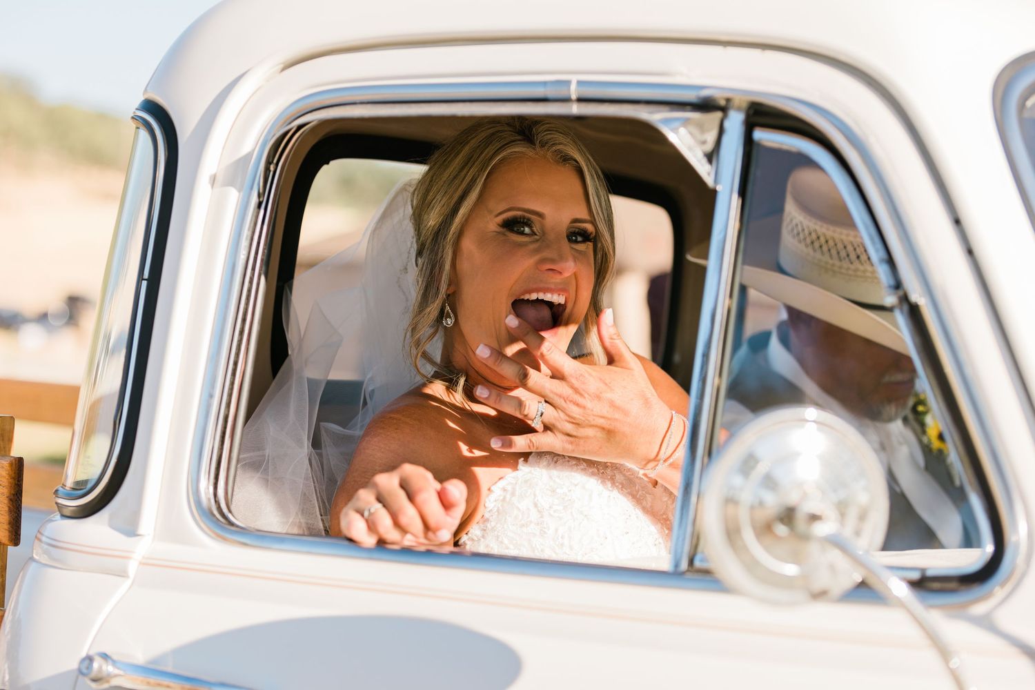 A group of women sit in vintage cars posing through windows in golden hour lighting at a bridal photo shoot.