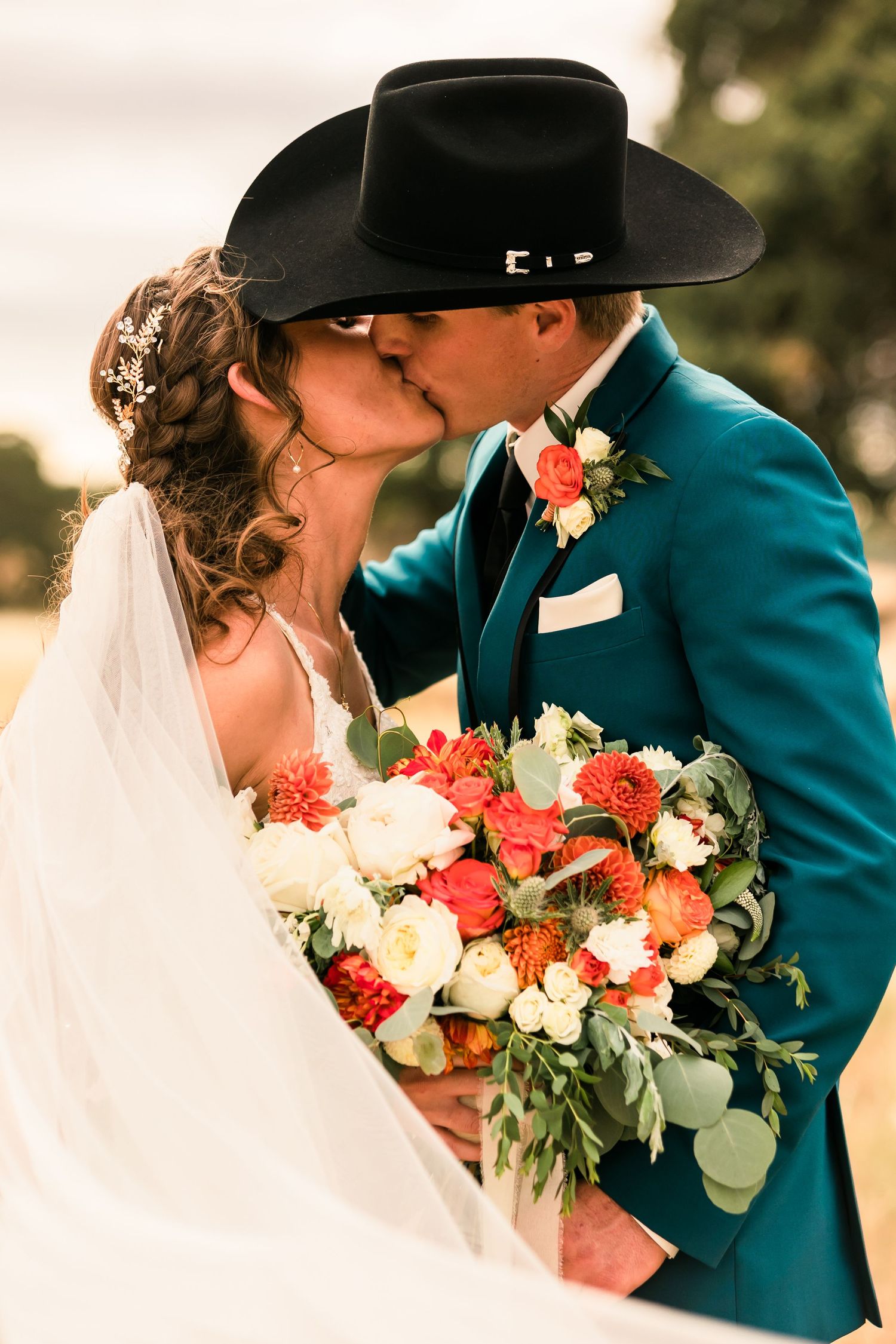 Couple in teal and black western attire sharing intimate moment with coral and white floral bouquet.